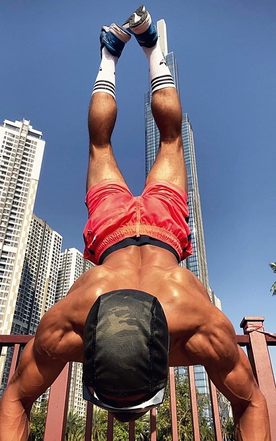 An athlete holding an inverted position supported on a park railing, with high-rise towers and open sky behind.